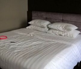 Unmade bed with white sheets and pillows in a dimly lit room.