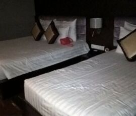 Two neatly made beds with white linens in a dimly lit room.