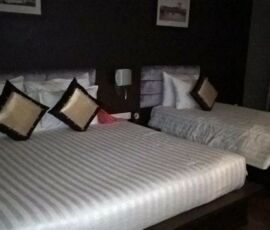Two neatly made beds with decorative pillows in a dimly lit room.