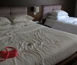 Two unmade beds with rumpled sheets and a red hanger on one bed.