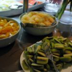 Three bowls of food and a plate of sliced cucumbers on a table.