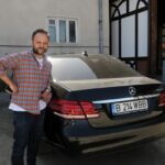 Man standing next to a black luxury car outdoors.