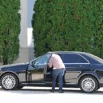 A man cleaning the side window of a black car on a sunny day.