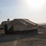 A small house with a slanted roof under bright sunlight in a barren area.