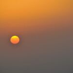 A vibrant orange sun sets in a hazy sky.