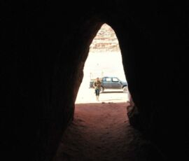 View from inside a dark cave with a white SUV parked outside in daylight.