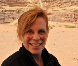 Smiling woman with short red hair in a desert landscape.