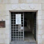 Entrance to an old stone building with a metal gate and informational signs.