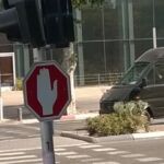 Pedestrians crossing a city street near a traffic sign and parked cars.