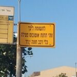 Street signs with directions in Hebrew and English under a clear sky.