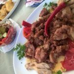 Grilled meat platter with fresh vegetables and sauces on a table.