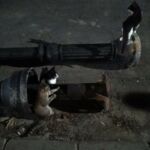 Two cats resting on a sidewalk at night near a bench.