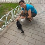 Person crouching to pet a small black and white dog on a paved path.