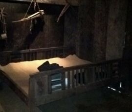 Dimly lit rustic bedroom with an old wooden bed and hanging light.